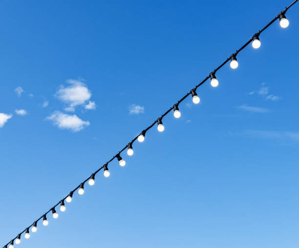 istock Lightbulbs hanging on wire over blue sky background 1826599974