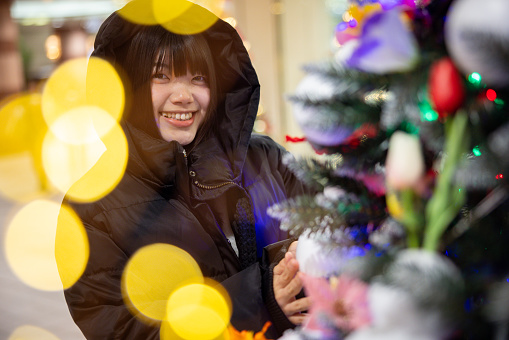 Portrait of young woman in hoodie standing with Christmas tree