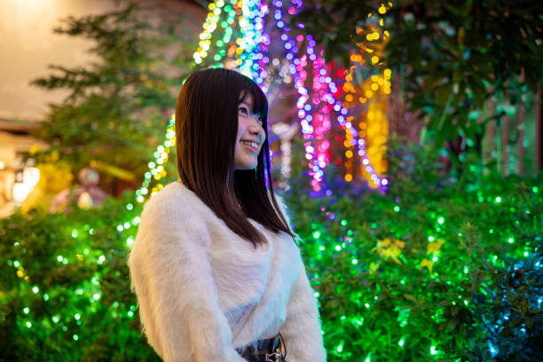 istock Young woman standing in front of Christmas lights - low angle view 1826601151
