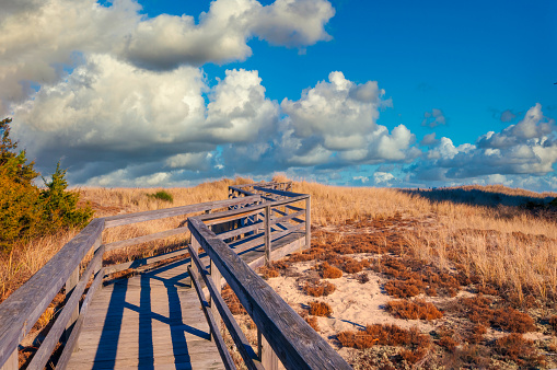 A wooden boardwalk zig zags across a sand dune as it leads to a sandy beach just over the hill.