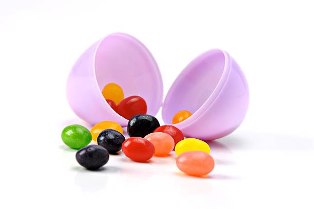 Jellybeans in Easter Egg Multi-colored jellybeans in a purple Easter egg isolated on white. jellybean stock pictures, royalty-free photos & images