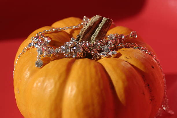 Close-up of a pumpkin's stem and upper portion. \n\n\nThe pumpkin is a muted orange-yellow color with a slightly rough, uneven texture. Visible are the prominent, dried, light brown stem segments emerging from the top, arcing slightly upward. \n\n\nThe background is out of focus, showing a pale, gray-white surface, likely a window or wall. A blurred, dark gray horizontal line is noticeable in the upper middle ground, suggesting a pane of glass or a similar flat surface partly visible beyond the pumpkin. The focus is primarily on the pumpkin and its stem, with the background becoming progressively less distinct.