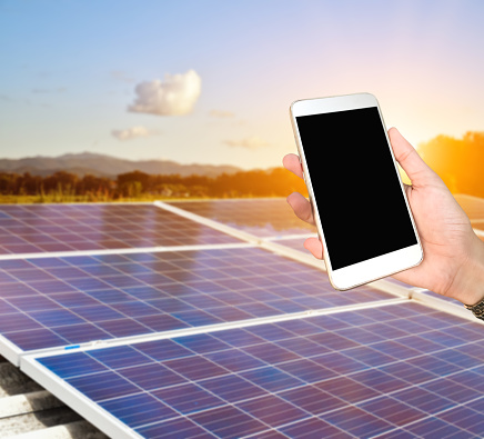 Closeup image of mobile phone which has blank screen holing in hand with blurred solar rooftop of the buildings background, concept for using digital devices with solarcell system.