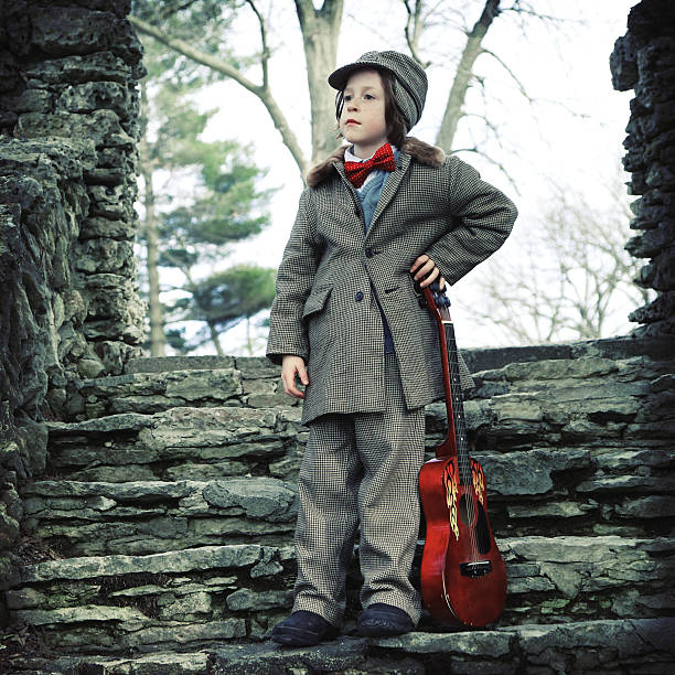 Adorable Little Musician with Suit, Bow Tie and Guitar "Adorable little boy in vintage hat and jacket and red bow tie stands with red guitar by stone pillar. Cropped square.Shot with Canon 1Ds Mark II, cross processed and color saturation reduced, vignette added, copy space." rockabilly boys stock pictures, royalty-free photos & images