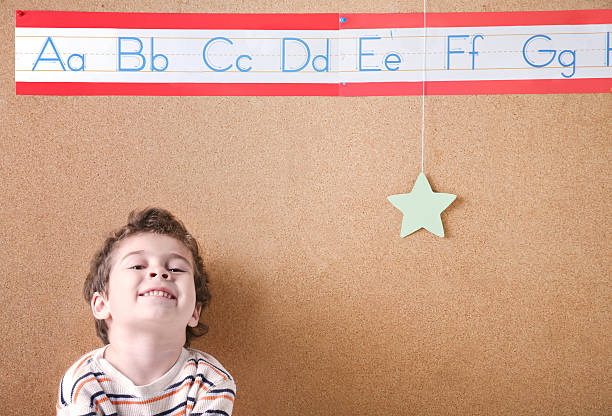 Star Student ABCs A smiling kindergarten boy sits against a cork board in the classroom. g star stock pictures, royalty-free photos & images