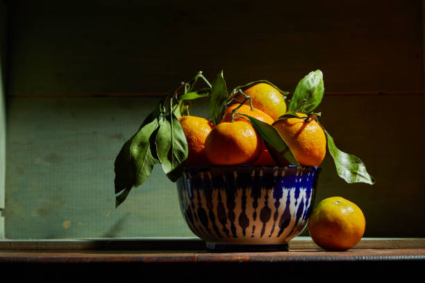 Fresh organic tangerines with leaves in bowl in bright sunlight with copy space. Still life with natural tropical fruit. stock photo