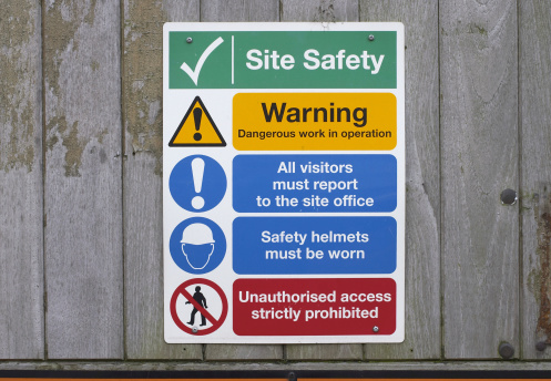Five notices in one: warning signs about safety on a building site, fixed to a wooden fence.