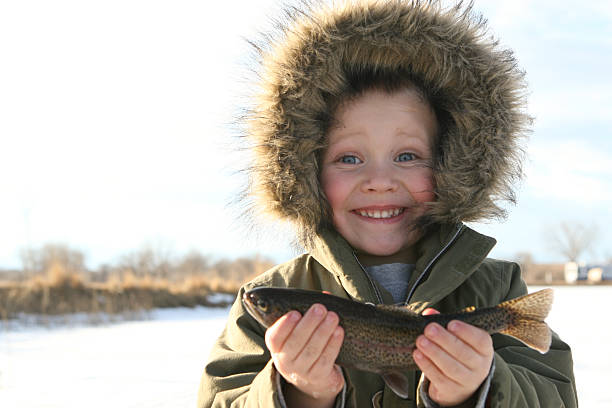 enfant de la pêche sous la glace en tenant son poisson - ice fishing photos et images de collection