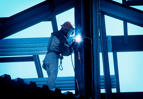 Iron worker welding an i beam on a high rise building