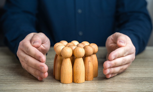 A man protects human figures with his hands. The concept of security and social protection. Health coverage benefits, retirement plans. Creating an environment where everyone feels secure and valued.