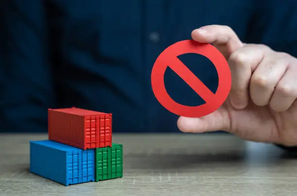 Photo of Shipping containers and prohibition symbol NO. Ban on import of goods. Sanctions and embargoes. Trade wars. Container shortage crisis. Blocking of cargo and blockade of trade routes.