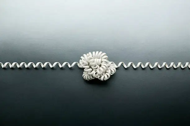Photo of Coiled telephone cord tied in a knot on gray background