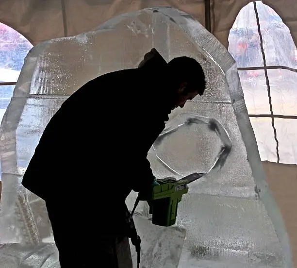 silhouetted male sculpting a block of ice with a chainsaw