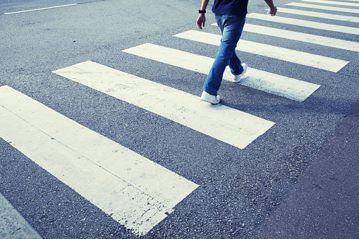 Man in jeans walking across a zebra crossing