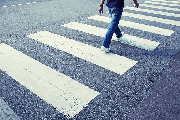 Photo of Man in jeans walking across a zebra crossing