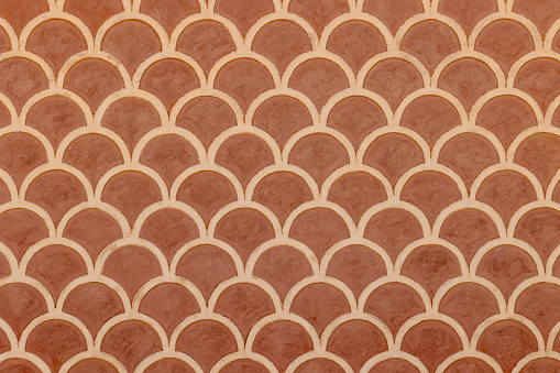 Fish scale repeating pattern on old red and beige fresco wall on street facade in Tarragona