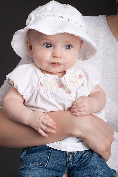 Cute baby girl wearing a white hat being held in arms.