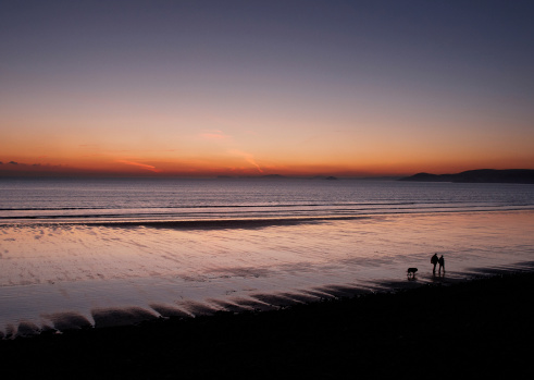 Irish Sea at dusk fiery sunset couple with dog