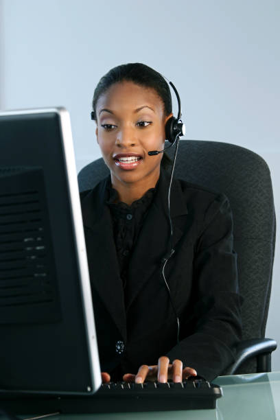 Help Desk Talking young woman (early twenties) wearing a headset and working on a computer - shot in studio modeldl stock pictures, royalty-free photos & images