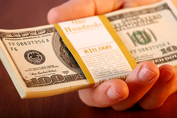 Close-up of mans hand holding out $10,000 stock photo