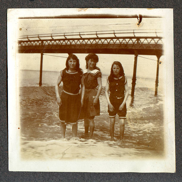 Edwardian girls by the seaside Vintage photograph of three young girls paddling in the sea during the Edwardian period. England circa 1900 to 1910. one piece swimsuit photos stock pictures, royalty-free photos & images
