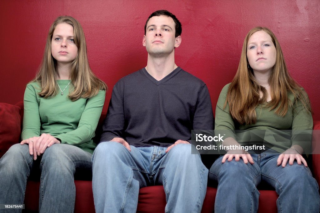 RedWall 3 young adults posed side by side on a red couch in front of a red wall Boredom Stock Photo