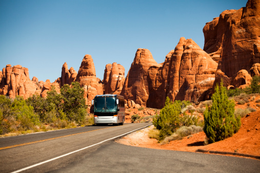 Motor coach drives tourists on vacation in the southwest USA red rock landscape in Arches National Park near Moab Utah