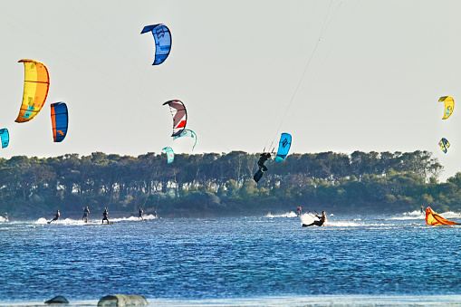 Smiling girl in a black tight-fitting wetsuit with pink and blue stripes rides on the waves with a blue parachute