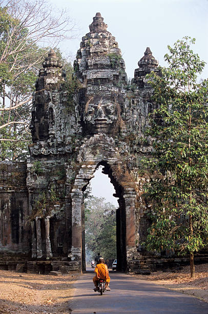 Angkor Wat Gate One of the amazing gateways to the ancient city of Angkor Thom (with huge Bayon faces staring down) - near Angkor Wat - hidden in the jungle of Cambodia in South East AsiaMonks in saffron coloured robes are a common sight in Cambodia - and scooters are the main means of transportation. angkor thom stock pictures, royalty-free photos & images