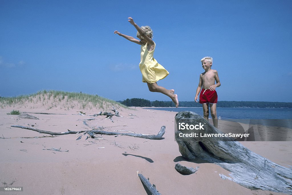 Crianças jogando e pulando em uma praia de areia - Foto de stock de Amarelo royalty-free