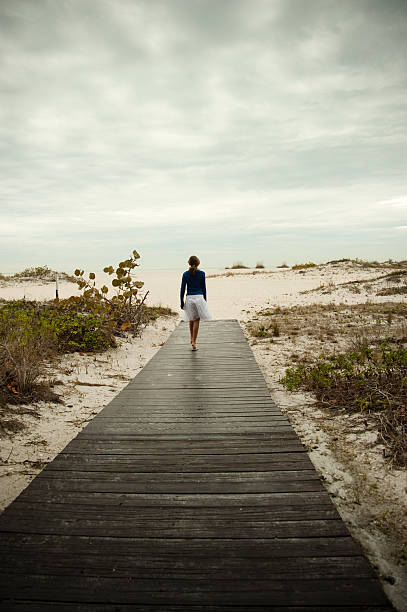 Walking toward the beach after rain. "A lonely young girl is walking on a wooden pier toward the beach after a light shower of rain. This was taken in Clearwater, Florida." clearwater stock pictures, royalty-free photos & images