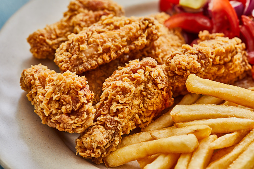 Fried chicken barbecue plates served on a blue rustic wooden table, with French fries and cola, representing a street food culture, city life and take out food indulgence culture, unhealthy eating and wellbeing