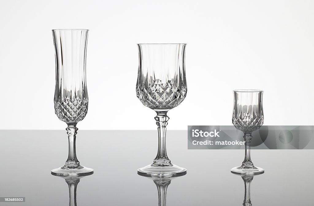 Lead cut glass crystal stemware "A champagne flute, wine glass and liqueur glass made out of cut glass (crystal glass or lead glass), on plain gray shiny surface with gray background" Crystal Glassware Stock Photo