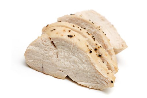 Sliced cooked chicken breast against white, topped with black pepper