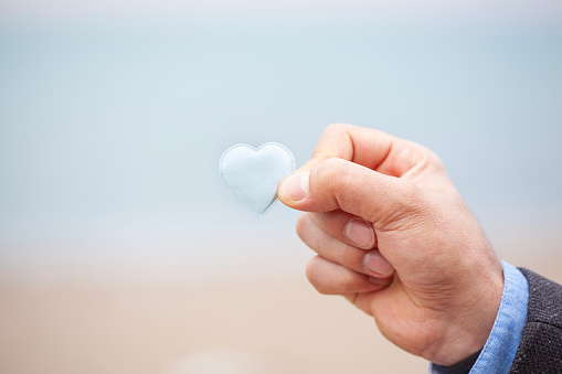 Man hand holding light blue heart. Young hand holding or giving a light blue heart, concept of family and donation or adoption, health care and medicine concept. Valentines Day concept. Breast Cancer Awareness concept.