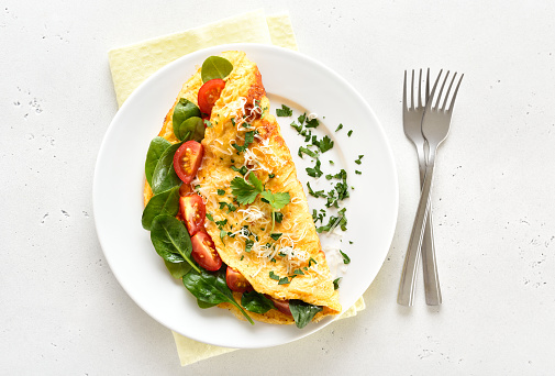 Stuffed omelette with tomatoes and spinach on light background. Top view, flat lay