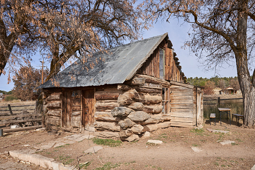 A old fashioned log cabin, labeled land office, sitting in southern Utah with a metal roof.
