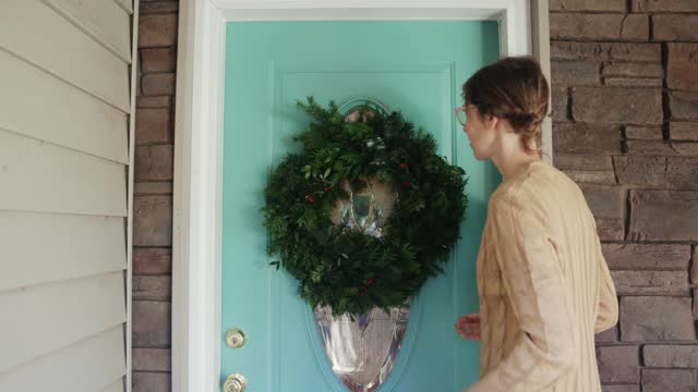 Woman Hangs Christmas Wreath on Front Door