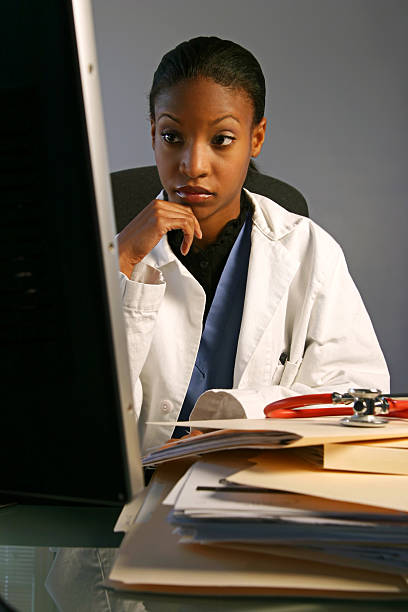 Young Doctor Thinking Young doctor (twenties) looking at computer in office modeldl stock pictures, royalty-free photos & images
