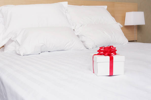 White gift box wrapped in red ribbon on a double bed stock photo