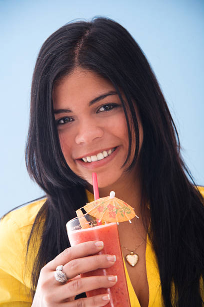 Young woman drinking a fruit smoothie on a blue background.