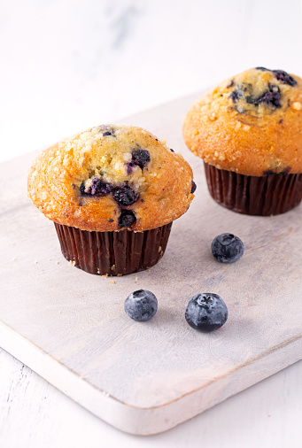 Fresh blueberry streusel muffins in a bright environment with fresh berries in the foreground; copy space