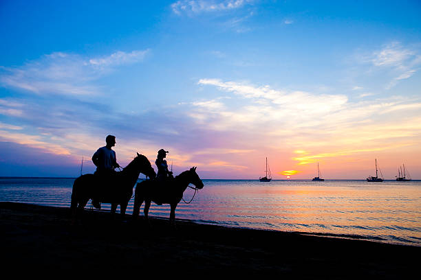 пара верховая езда на пляже на закате - trail ride стоковые фото и изображения