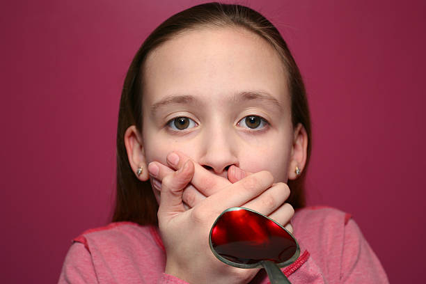 Child covering mouth when shown spoonful of cough syrup stock photo