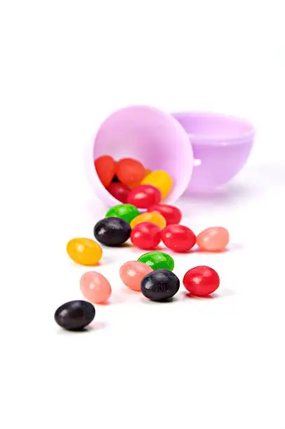 Multi-colored jellybeans in a purple Easter egg isolated on white.