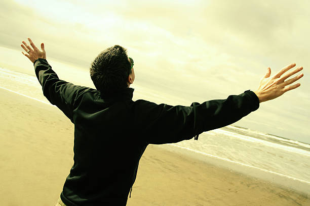 A man worshipping with his hands in the air on a beach stock photo