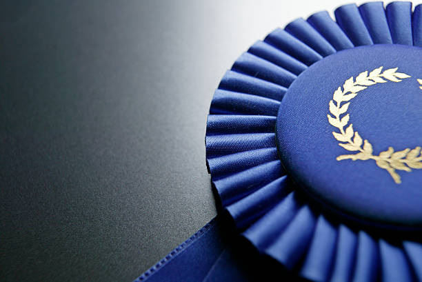 Blue ribbon rosette on dark gray graduated background Close up of blue ribbon with room for copy. award ribbon photos stock pictures, royalty-free photos & images