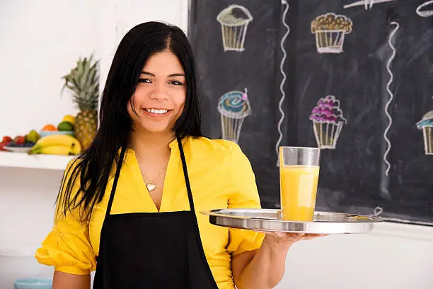 Photo of Cafe Employee Standing & Holding Orange Juice on a Tray