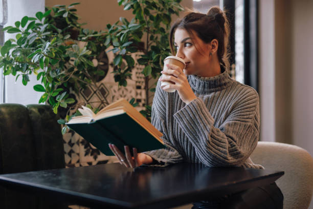 istock Young woman reading book sitting in a cafe drinking coffee 1826955498
