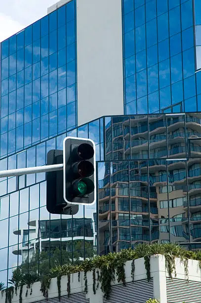 Traffic lights on green with tall glassy office building in the background